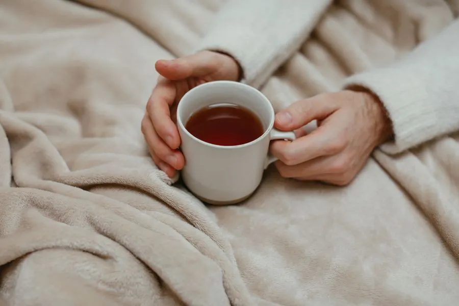 Hände halten eine warme Teetasse auf einer weichen Decke